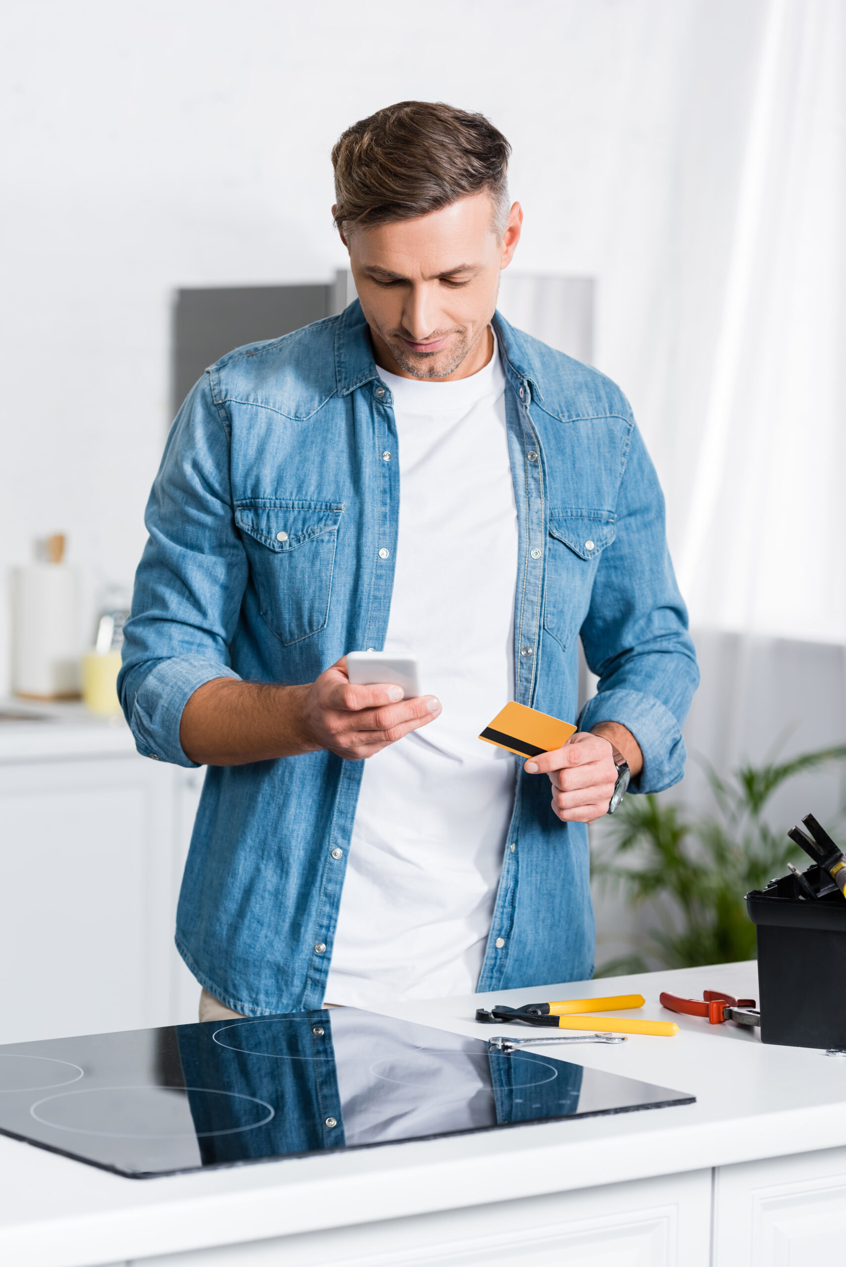 handsome man holding smartphone and credit card near tool box
