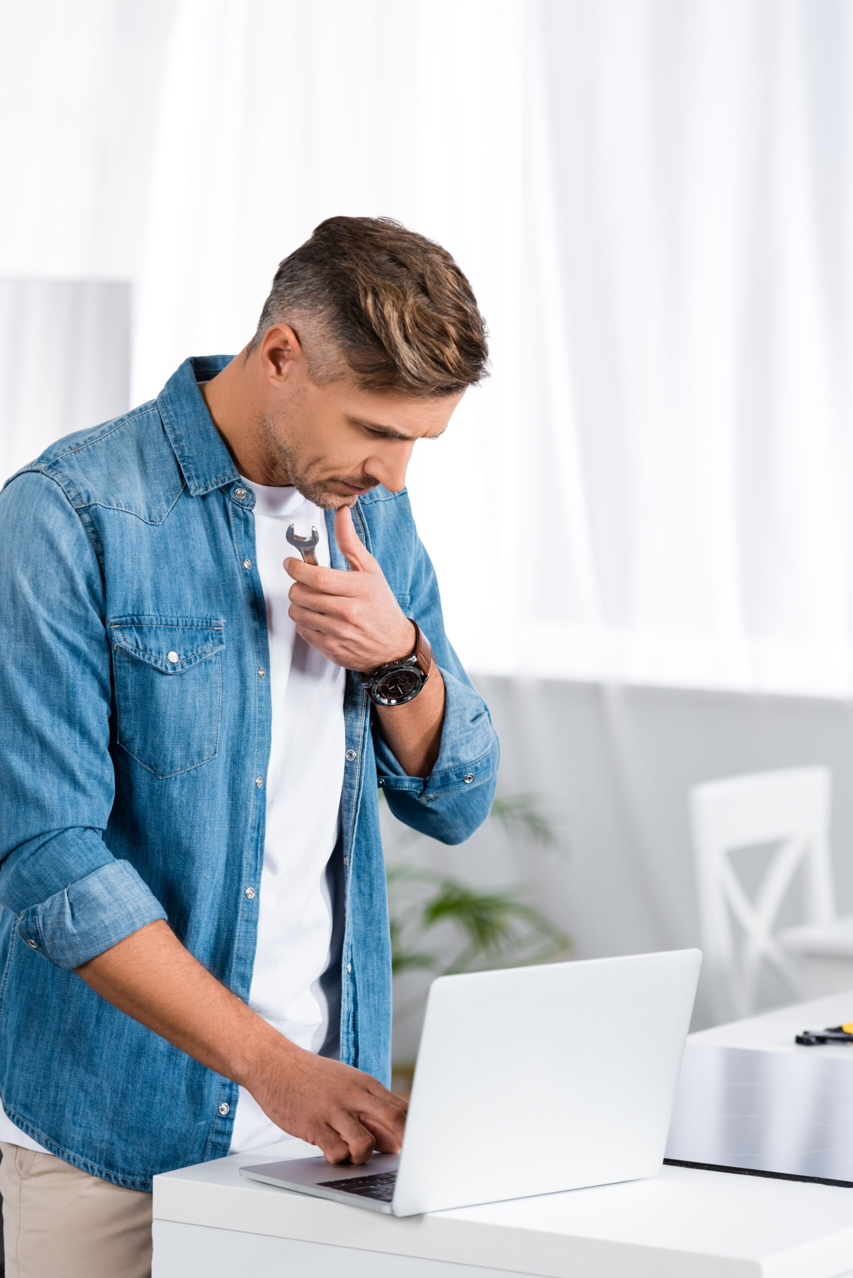 thoughtful man holding repair tool and using laptop